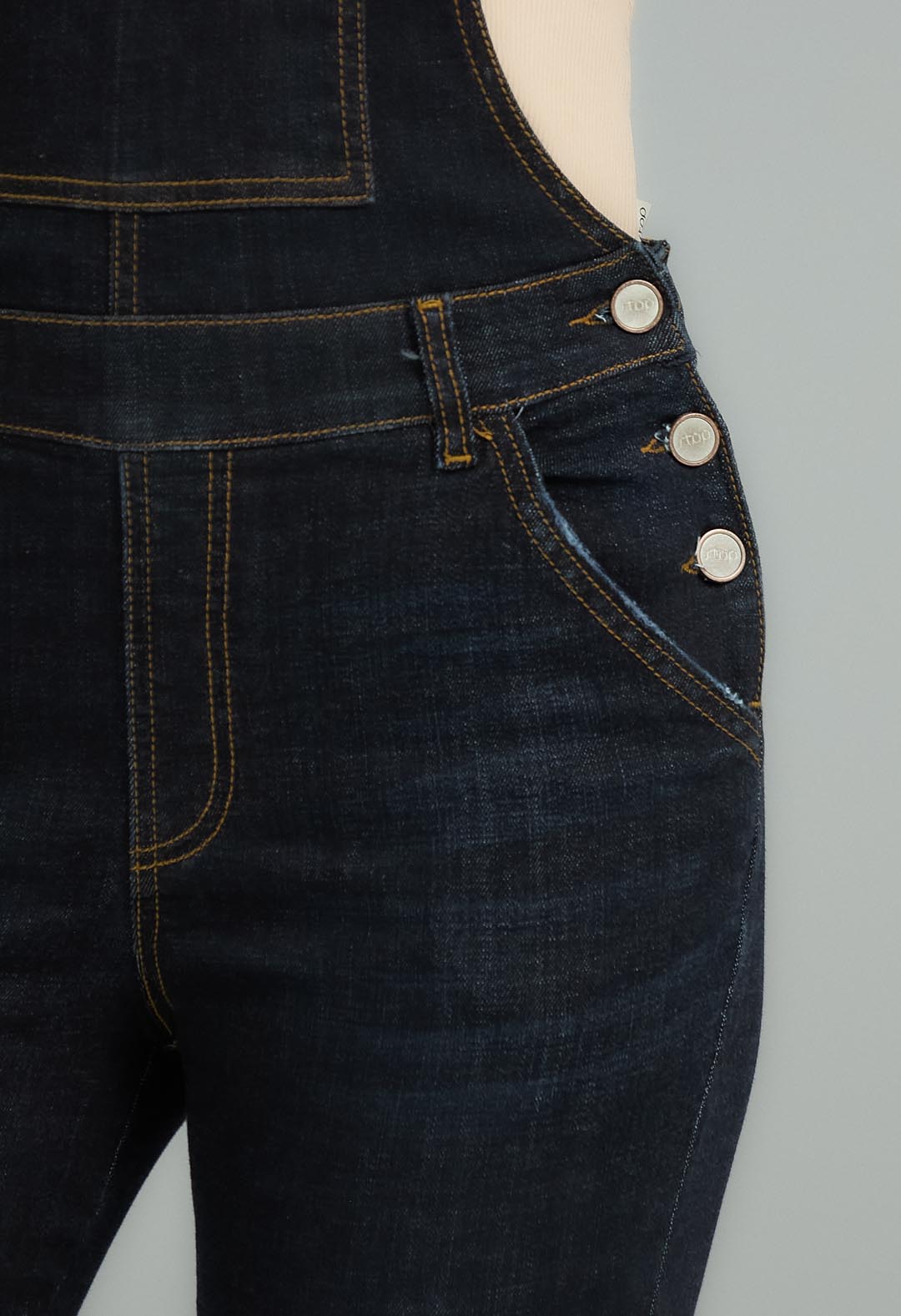 Mujer con overall oscuro en denim de la marca Stop, viste un estilo casual y moderno, en una pose de pie frente a fondo neutro.